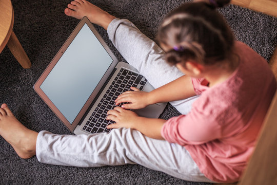 Young smart baby girl playing at home and using laptop.