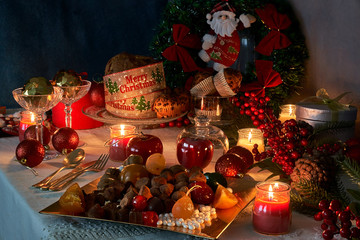 Christmas or New Year in the light of candles with sweets, red and gold ornaments specific for these dates on a white thread tablecloth background.