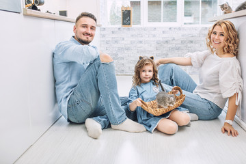 Family father, mother and sweet daughter happy together with little fluffy kittens in the kitchen in a bright home interior