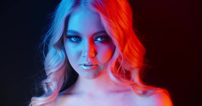 Beautiful caucasian girl wearing glowing makeup in neon light sensually looking at camera and pressing finger against her lips - nightlife, cybcerpunk concept 4k footage