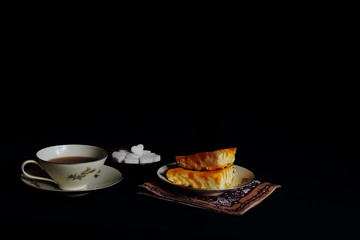 Delicious cottage cheese and pumpkin homemade pie, curly white sugar and cup of aromatic tea on black background. Concept of food, organic food, dessert, breakfast, gourmet.