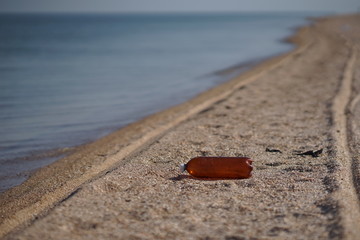 Empty plastic bottle lying on the sea beach. Environmental pollution. Tire tracks on the sand.