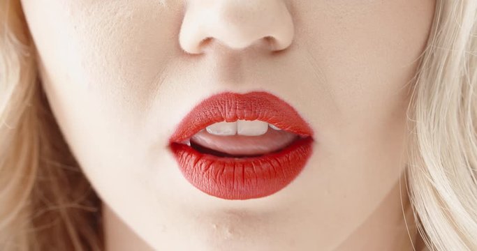 Close up shot of sensual blonde girl seductively licking and biting lips with bright red lipstick 4k footage