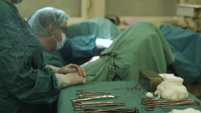 Nurse hands in gloves adding instruments team of surgeons during operation in operating room, close-up.