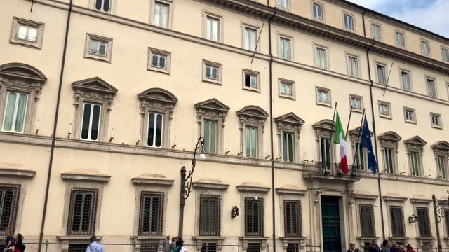 Facade of Palazzo Chigi (Chigi Palace), seat of the Italian government and prime minister at Piazza Colonna in Rome with people walking on a partly cloudy day. Panning movement from right to left
