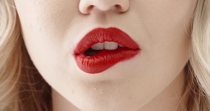 Close up shot of sensual blonde girl seductively licking and biting lips with bright red lipstick 4k footage