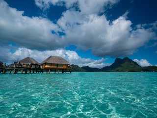 Luxury overwater villas on blue lagoon, white sandy beach and Otemanu mountain at Bora Bora island,...
