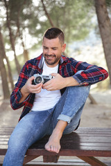 Hombre joven y apuesto con cámara analógica tomando fotos en medio de la naturaleza.	