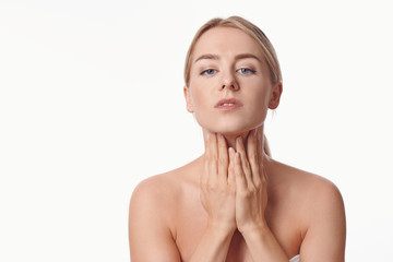 Beautiful young woman with bare shoulders massaging her throat with her hands in the morning to...