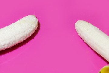 Two bananas on pink or purple background, one banana on left, another on right. Copy space between fruits