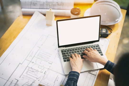 Top view, Architect or engineer hands working on blueprint plans with a laptop and pencil a ruler, calculator, and engineering tools. Architect or engineer working on blueprint in office.