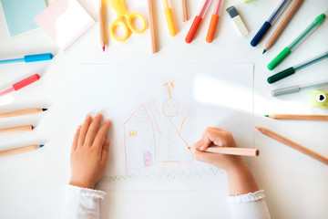 Close up of child's hands drawing at white paper within colorful pens and pencils.