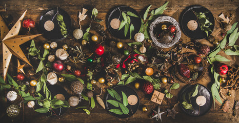 Christmas or New Year holiday celebration party table setting layout with decorative fur tree toys, garland, ropes, candles, glass balls, wreaths over dark wooden table background,top view