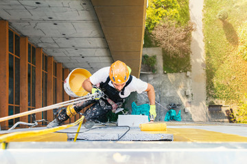 Industrial climber hanging on the rope while painting the exterior facade wall of the tall apartment building. Industrial alpinism concept image