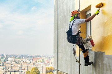 Industrial rope access worker hanging from the building while painting the exterior facade wall....