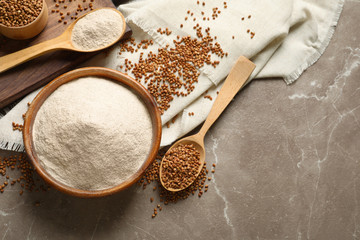 Flat lay composition with bowl of buckwheat flour and grains on grey marble table. Space for text