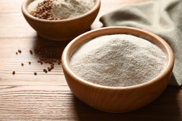 Bowl of buckwheat flour on wooden table, space for text