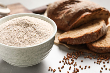 Bowl of buckwheat flour, grains and bread on grey table, space for text
