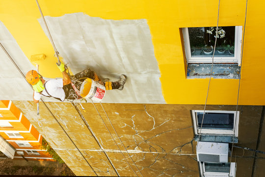 Industrial rope access worker hanging from the building while painting the exterior facade wall. Industrial alpinism concept image. Top view