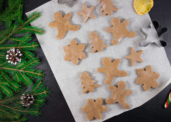 Carved figures of gingerbread dough on parchment, cooking gingerbread, Christmas tree branches. Flat lay, black background. Merry Christmas.
