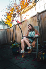 Girl in brown cardigan writing in book on chair on patio