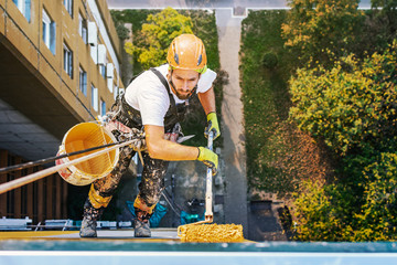 Industrial rope access worker hanging from the building while painting the exterior facade wall. Industrial alpinism concept image. Top view