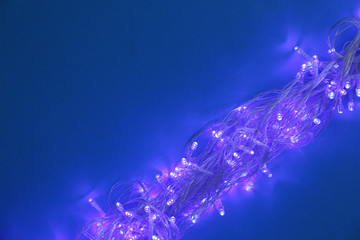 Glowing Christmas lights on dark blue background, top view. Space for text