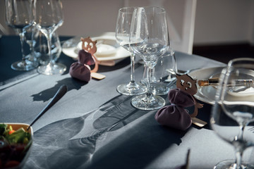 Glasses, flowers, fork, knife served for dinner in restaurant with cozy interior,