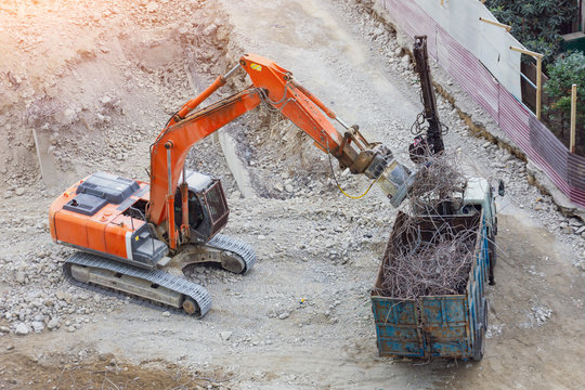 Loading metal reinforcement at a destroyed building with an excavator with a magnet.