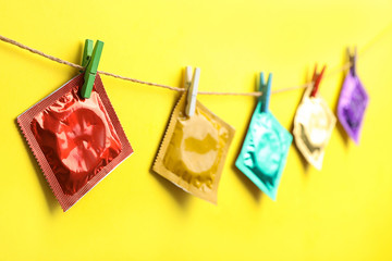 Colorful condoms hanging on clothesline against yellow background. Safe sex concept