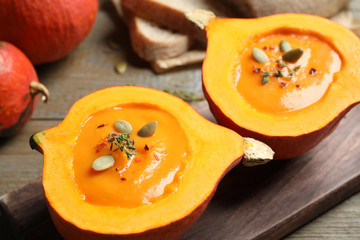 Tasty cream soup in pumpkin halves on wooden table, closeup