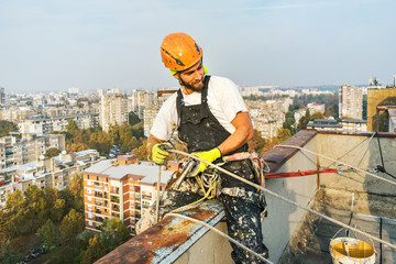 Industrial rope access worker hanging from the building while painting the exterior facade wall. Industrial alpinism concept image. Top view