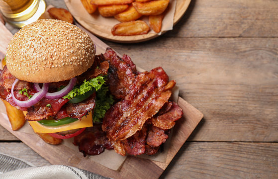 Composition with juicy bacon burger on wooden table, above view. Space for text