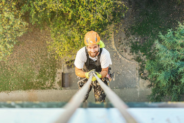 Industrial rope access worker hanging from the building while painting the exterior facade wall....