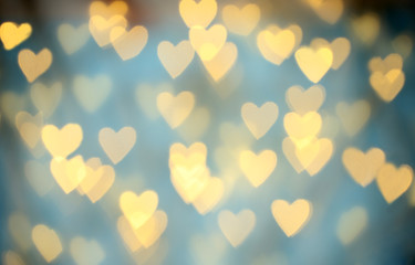 Blurred view of beautiful gold heart shaped lights on light blue background