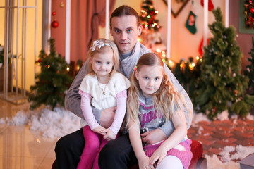 father and two daughters in Christmas decorations smiling and hugging