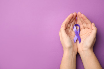Woman holding purple ribbon on lilac background, top view with space for text. Domestic violence...