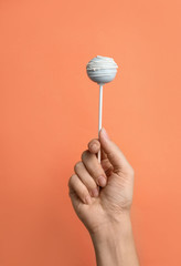 Woman holding sweet cake pop on coral background, closeup