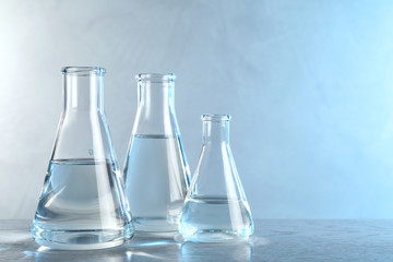 Laboratory glassware with liquid samples for analysis on table against toned blue background, space...