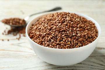 Bowl of uncooked buckwheat on white wooden table
