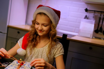 Concept: Christmas shopping.Young cute girl sitting at a table with Christmas gifts. Young lady is wrapping gifts. Girl opens gifts. Home decor in the background.