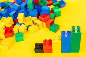 Bar graphs plastic building blocks toy bricks on yellow background.