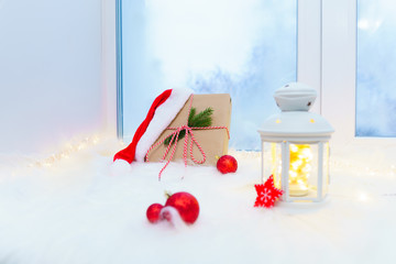 Gift box with Christmas decorations on a white windowsill near a blue window.