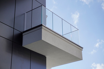 one open balcony or terrace on the facade of a concrete modern house against a background of blue sky with white clouds.