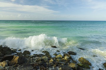 Big wave in Caribbean sea is breaking the coast. Turquoise sea water and blue sky. Eagle Beach of Aruba Island.  Beautiful nature background.