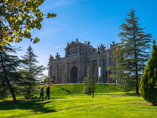 Fototapeta na wymiar Replica of the Puerta de Alcala in Madrid, in the Europa park of Torrejon de Ardoz, surrounded by trees and a beautiful blue sky in the background