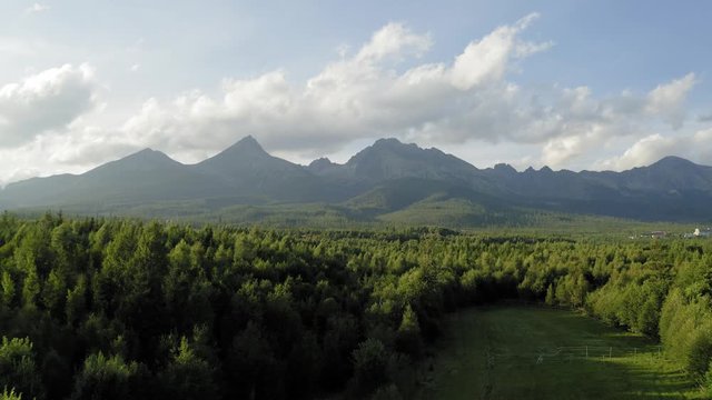 Aerial rising over magical forest with mountains on background at golden hour