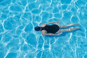 Young woman in cap sports swimsuit swimming underwater in blue outdoor pool