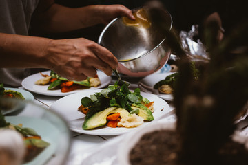 Male hands put green and fresh salad on plates in the kitchen. Homeliness and healthy dinner with friends at home