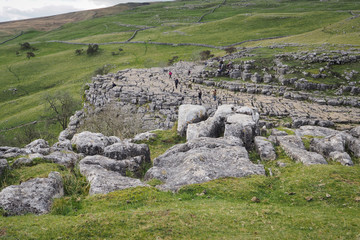 Fototapeta na wymiar The dramatic fissured limestone pavement geology high above Malham Cove set against green fields and dry stone walls, Yorkshire Dales, UK